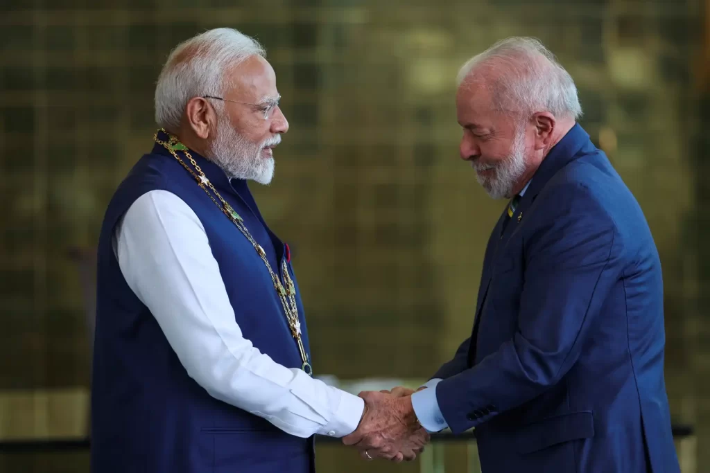 Primeiro-ministro Narendra Modi e então-presidente Jair Bolsonaro em um aperto de mãos durante encontro oficial, com expressão cordial. Foto capturada em um ambiente formal, destacando o relacionamento diplomático entre Índia e Brasil.