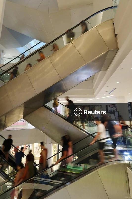 Foto de pessoas usando escadas rolantes em shopping center movimentado, com várias pessoas passeando e fazendo compras.