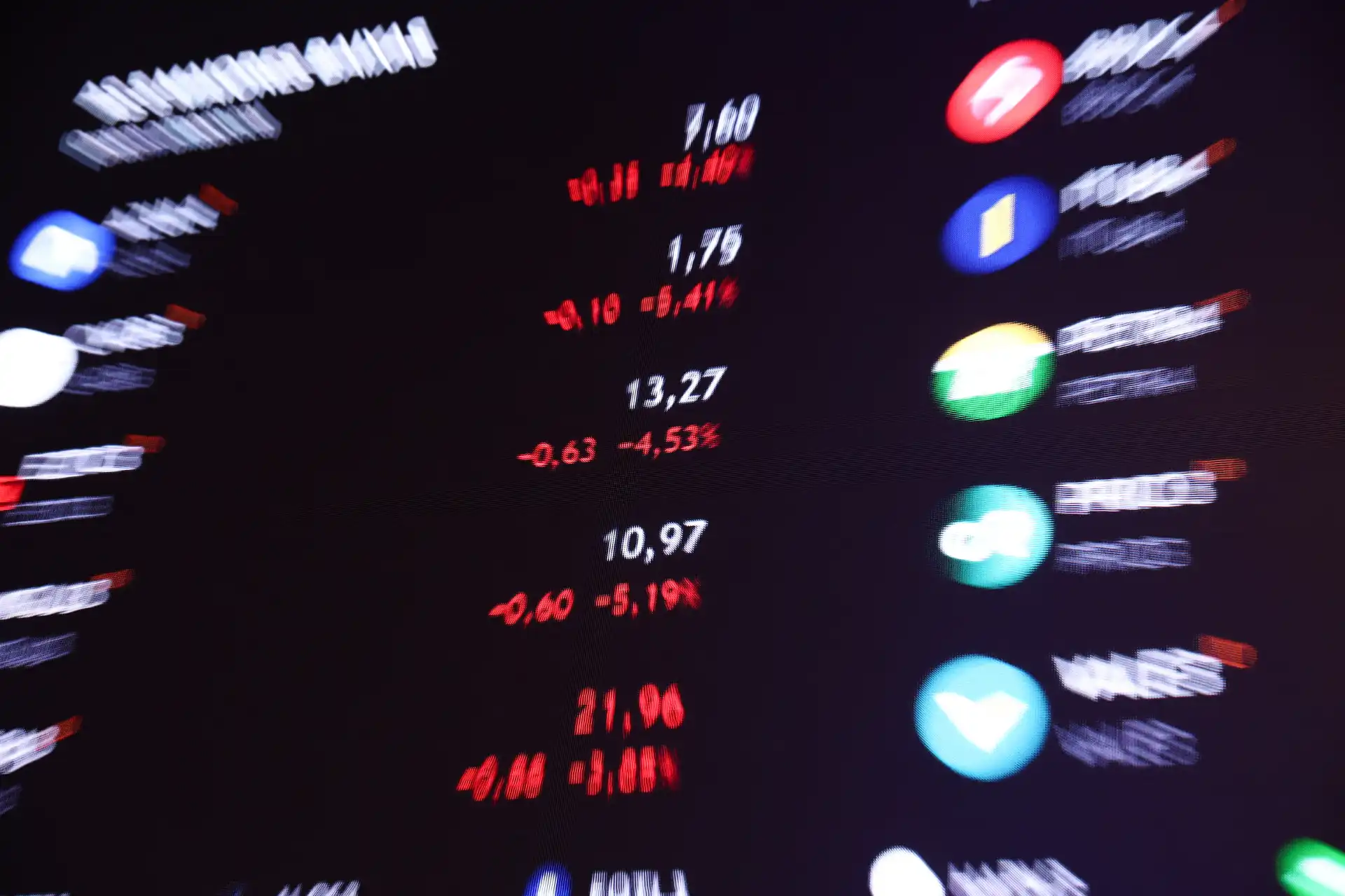 Imagem de tela de negócios financeiros exibindo cotações de ações, índices e moedas em uma plataforma de trading, com números em destaque em cores variadas.